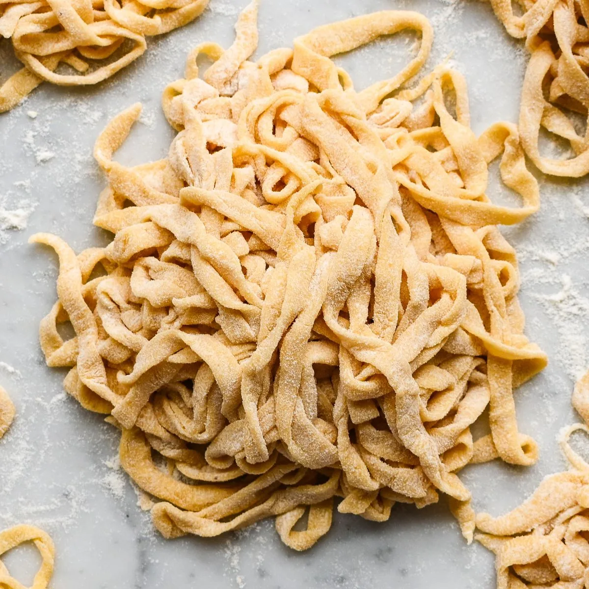 Floured nests of fresh sourdough pasta noodles on a marble surface, ready to cook or store for later use.