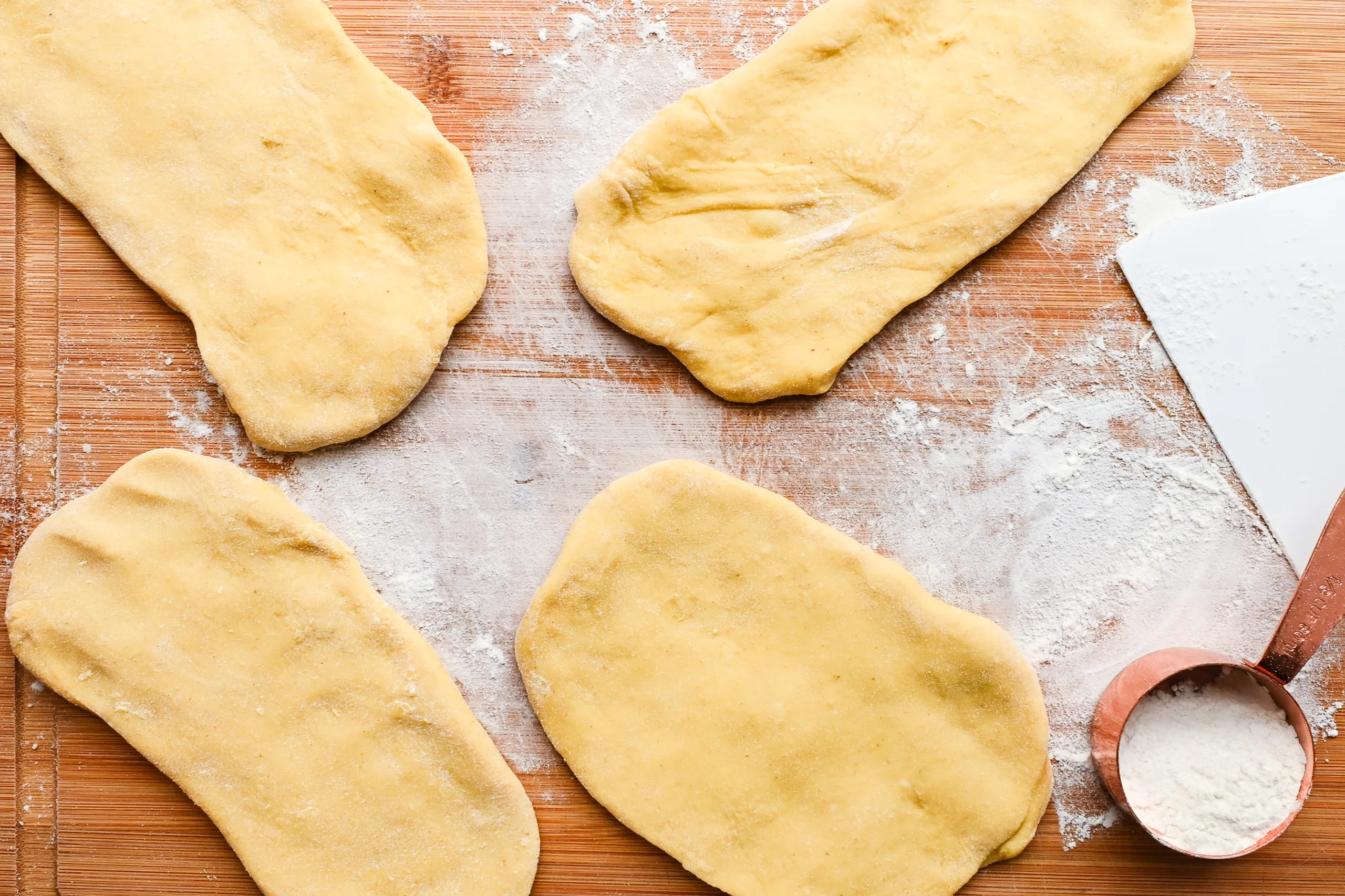 Rolled sheets of sourdough pasta dough resting on a floured wooden board, ready to be cut into noodles.
