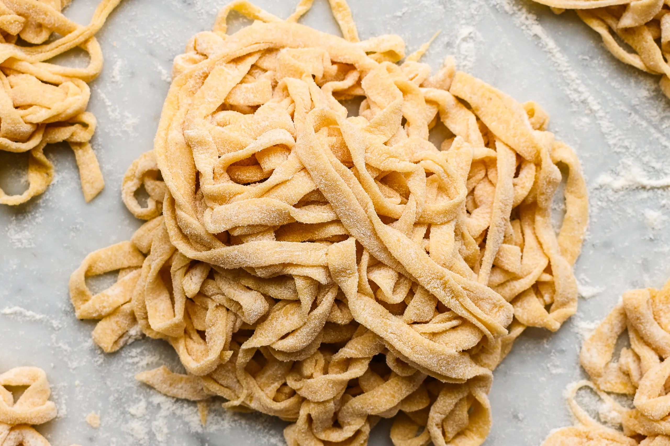 Floured nests of fresh sourdough pasta noodles on a marble surface, ready to cook or store for later use.