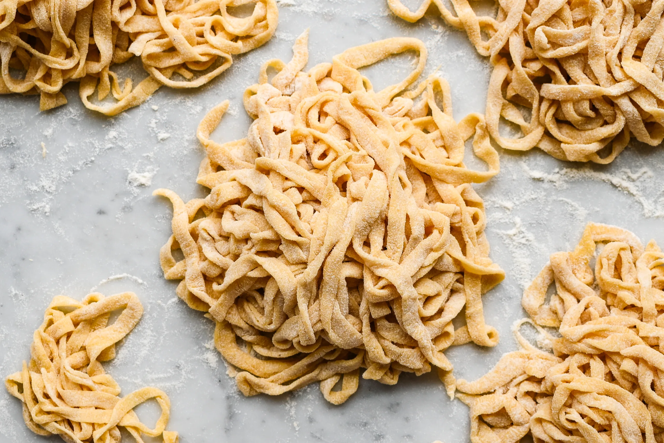 Floured nests of fresh sourdough pasta noodles on a marble surface, ready to cook or store for later use.