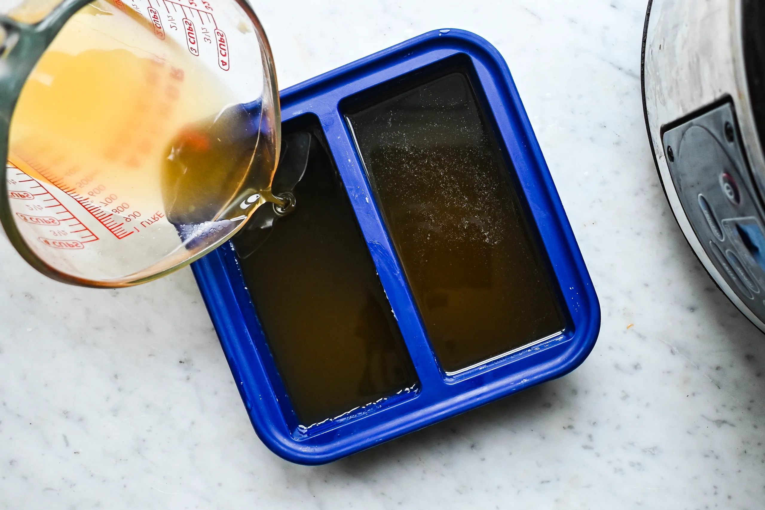 Pouring melted beef tallow into a blue silicone mold to cool and solidify for skincare use.