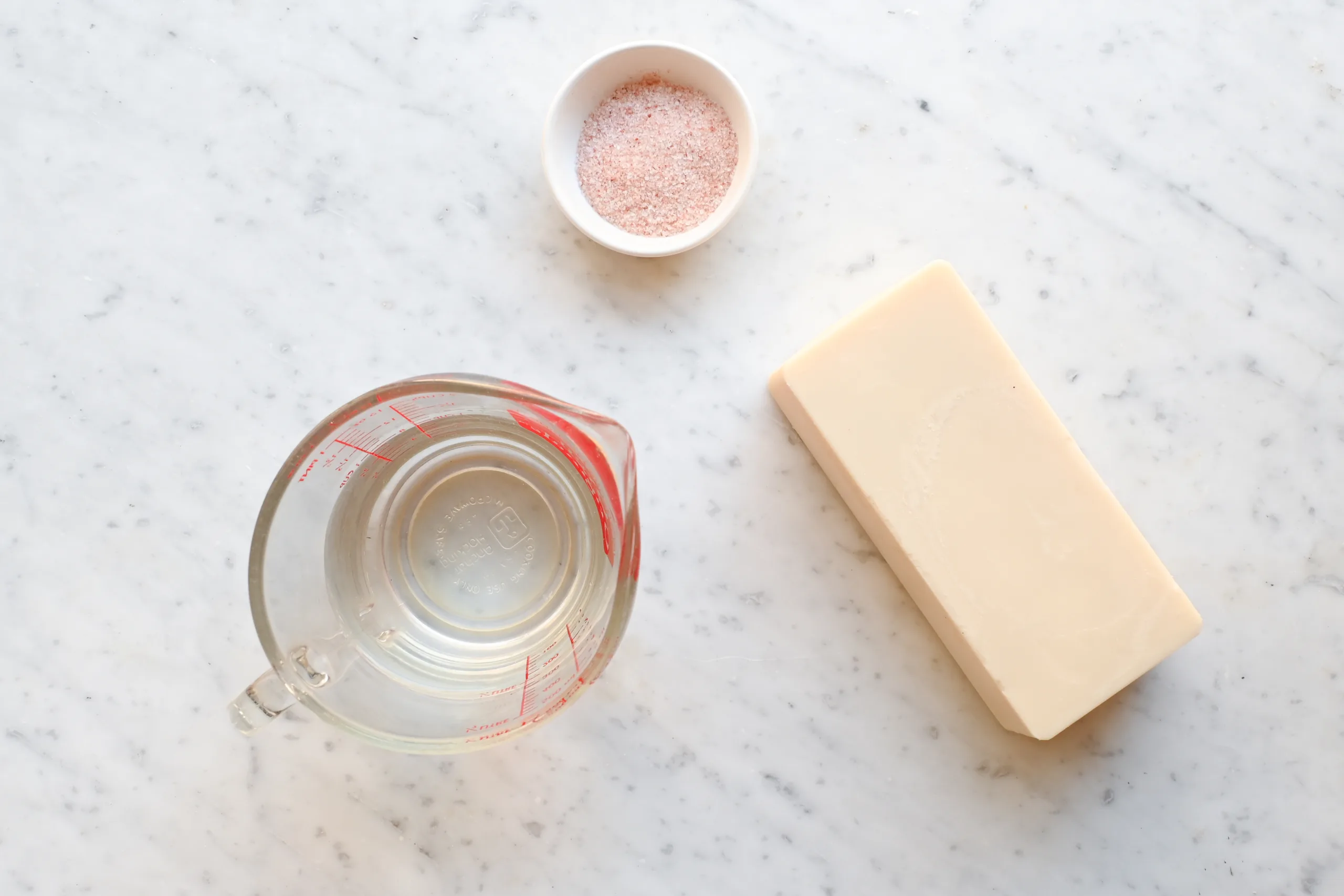 Beef tallow purification ingredients — solid tallow, salt, and water — arranged on a marble countertop.