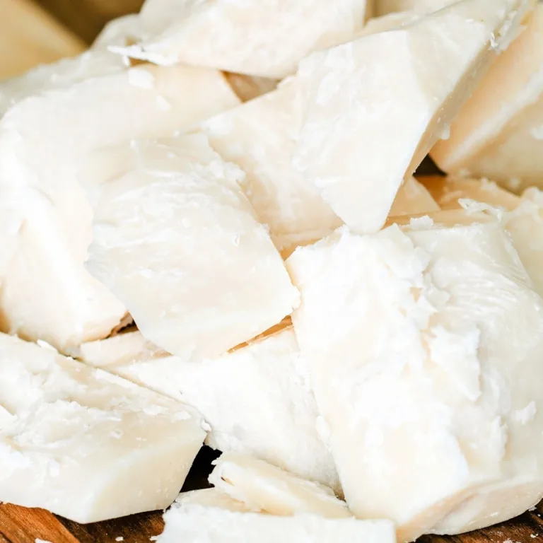 Close-up of creamy white chunks of beef tallow on a wooden board, showcasing the natural texture before purification for skincare use.