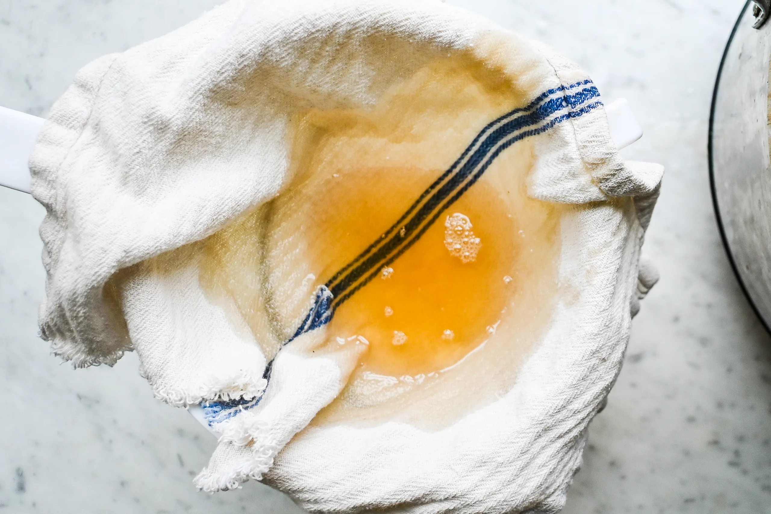 Straining melted tallow through a cloth-lined sieve to remove impurities during purification.