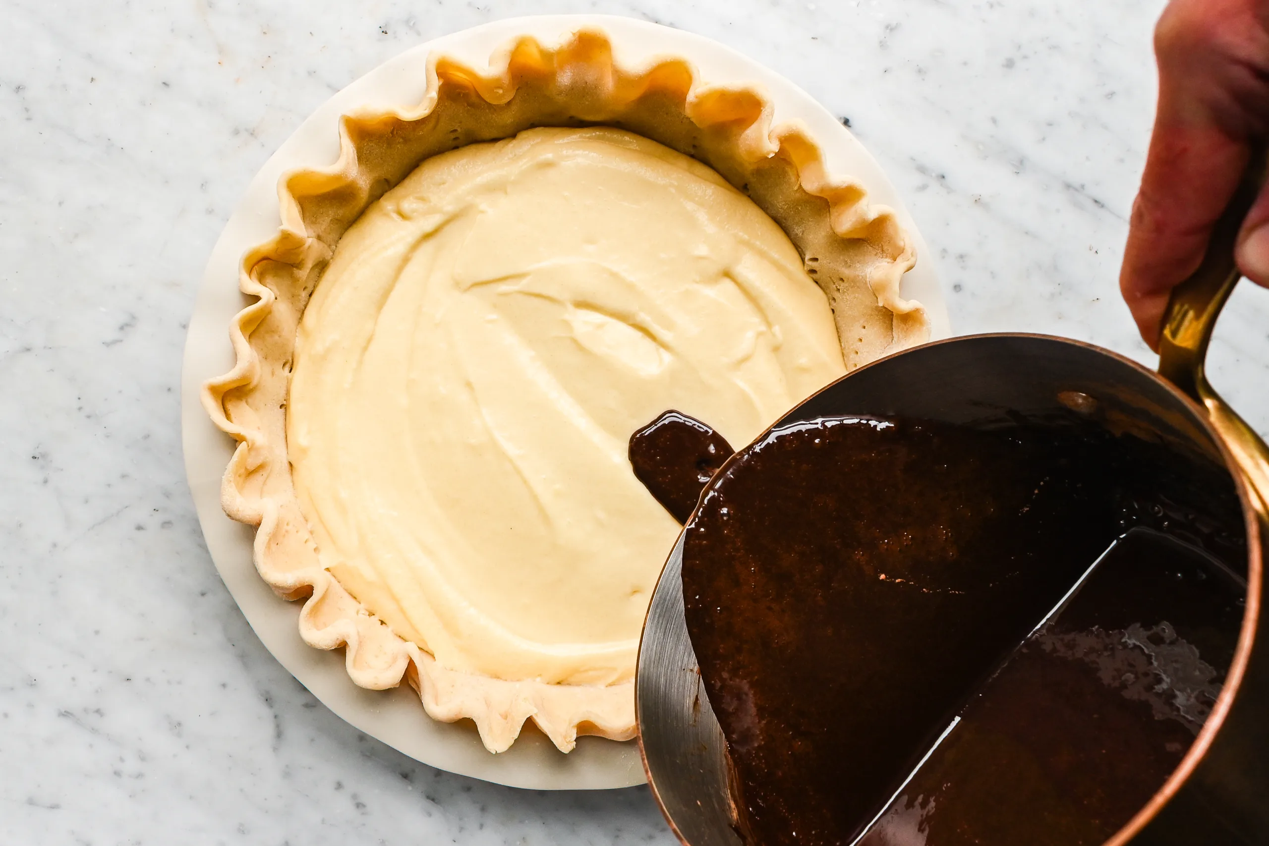 Pouring homemade chocolate syrup over vanilla cake batter in a pie crust for traditional Funny Cake.