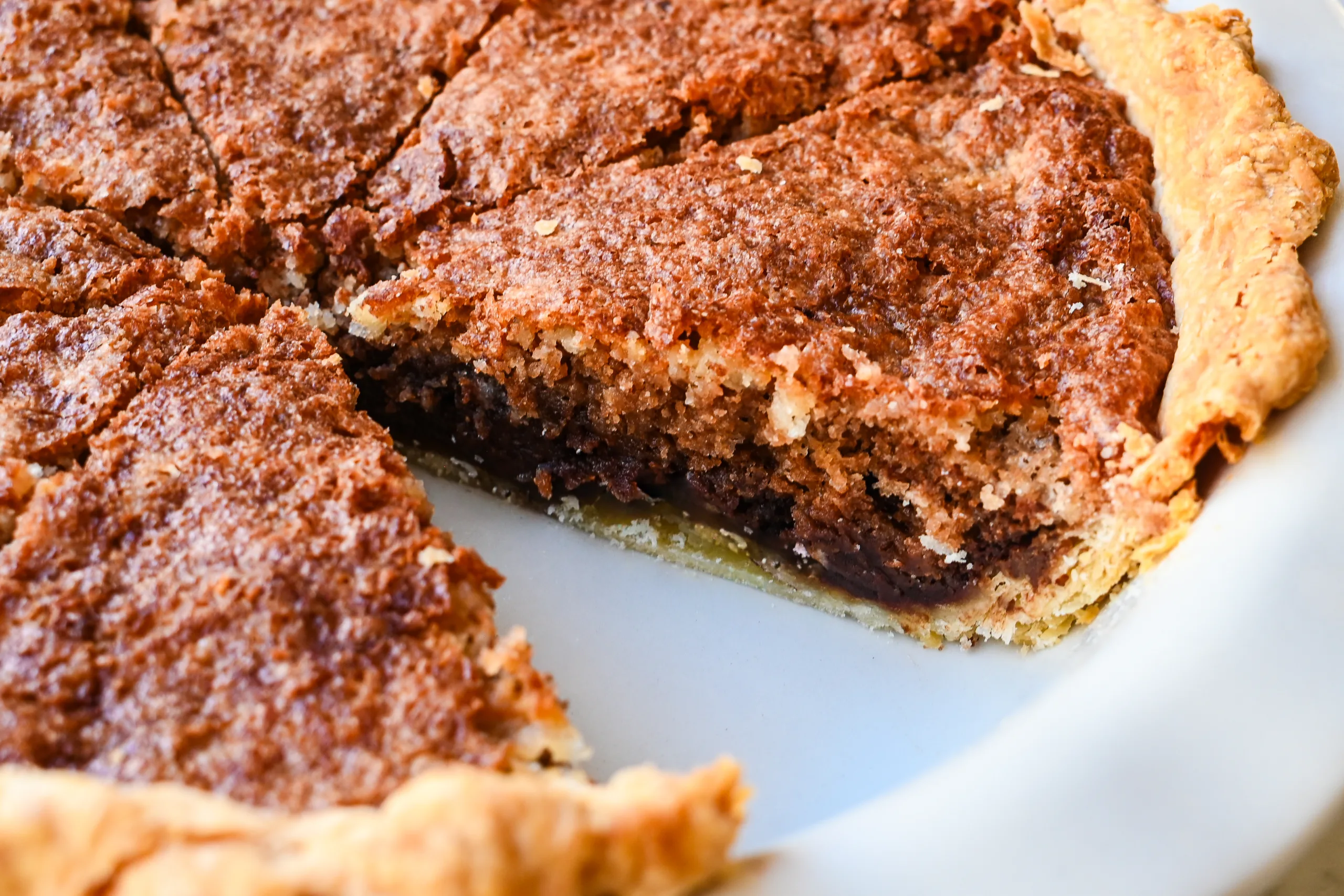 Close-up of Pennsylvania Dutch Funny Cake with a slice cut to show the rich chocolate layer baked beneath the vanilla cake inside a flaky pie crust.