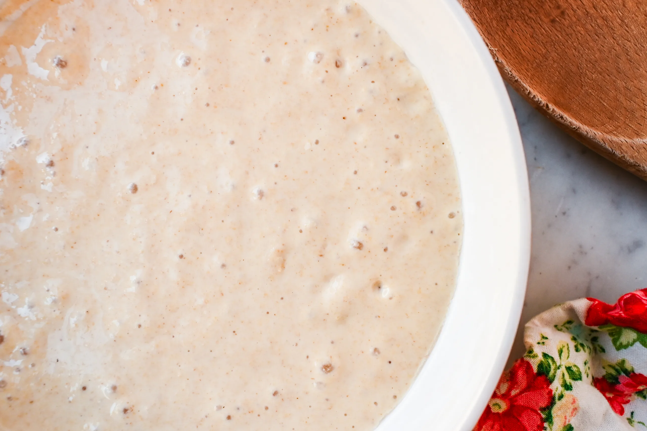 Freshly stirred sourdough discard in a ceramic bowl on a kitchen counter.