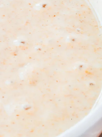 Creamy, lightly speckled sourdough starter in a white bowl, showing small bubbles forming across the surface as it ferments.