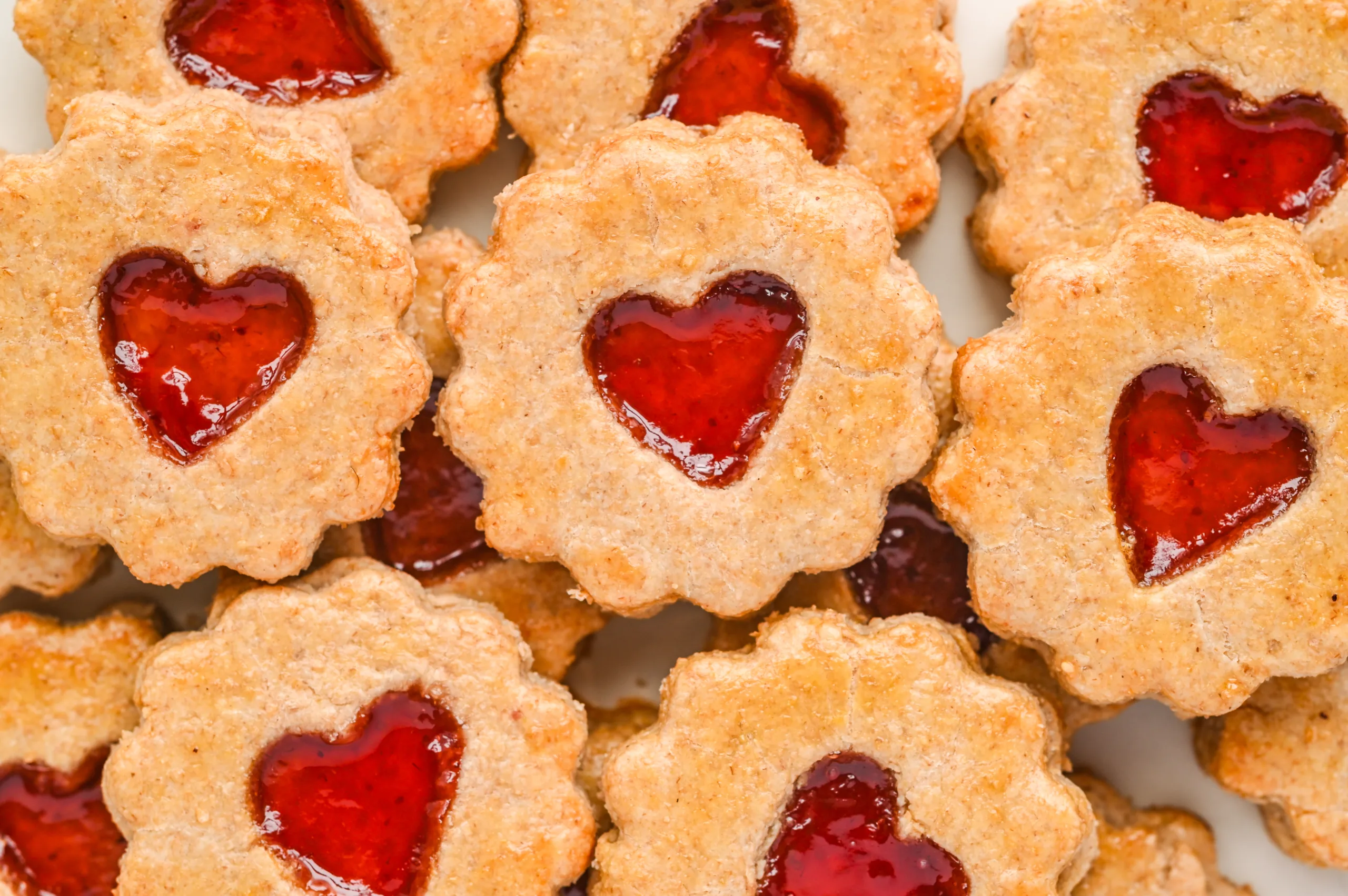 Old-fashioned pie crust cookies stacked closely together, showing the flaky edges and glossy heart-shaped jam centers.