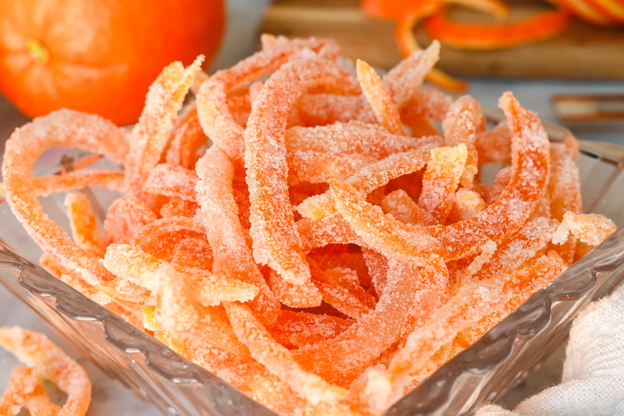 Close-up of sugar-coated candied orange peels piled in a small glass dish, showing their soft texture and sparkling crystallized sugar coating made using an old-fashioned method.