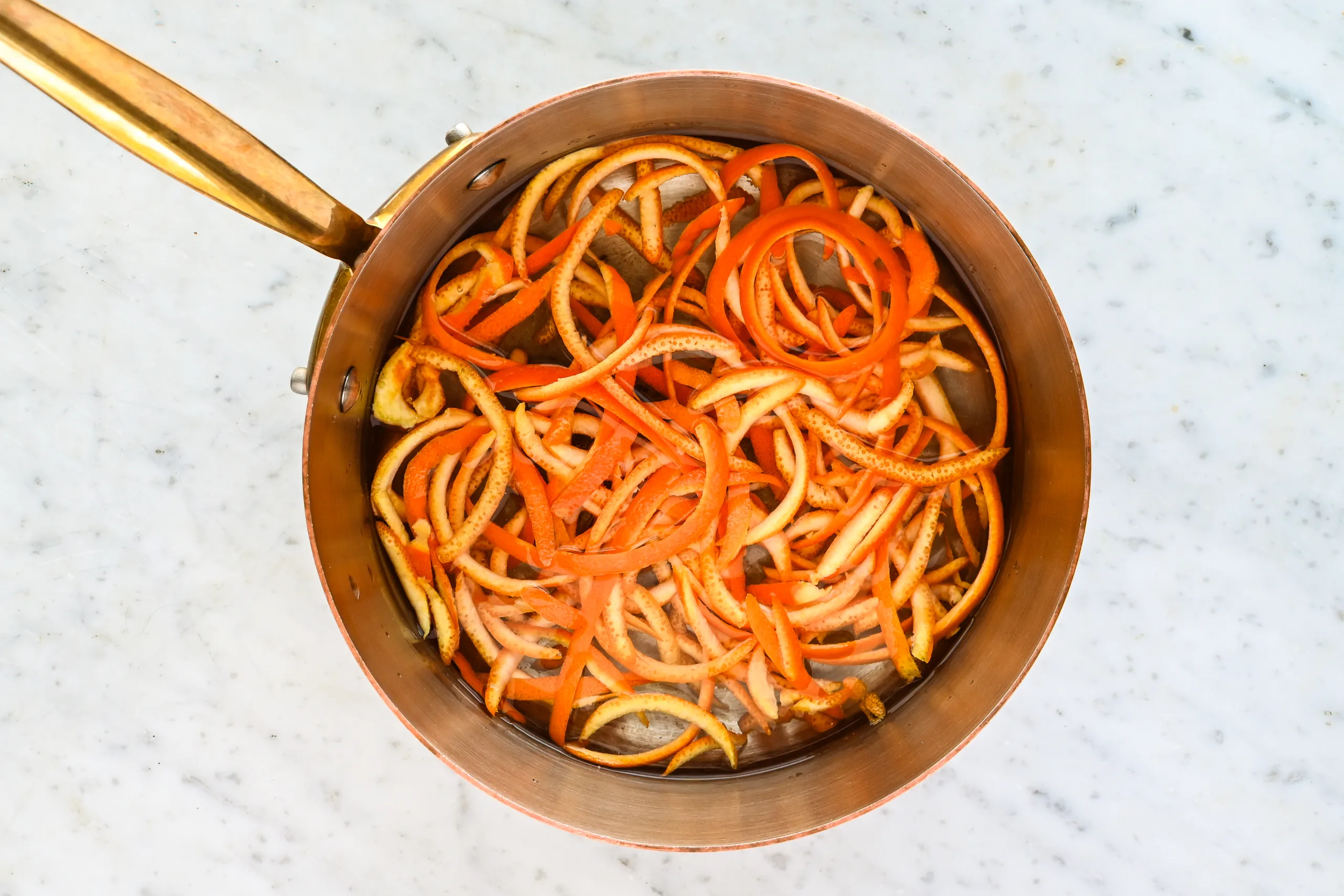 Thinly sliced orange peels simmering in a saucepan of water, an early step in the traditional candied orange peel process.