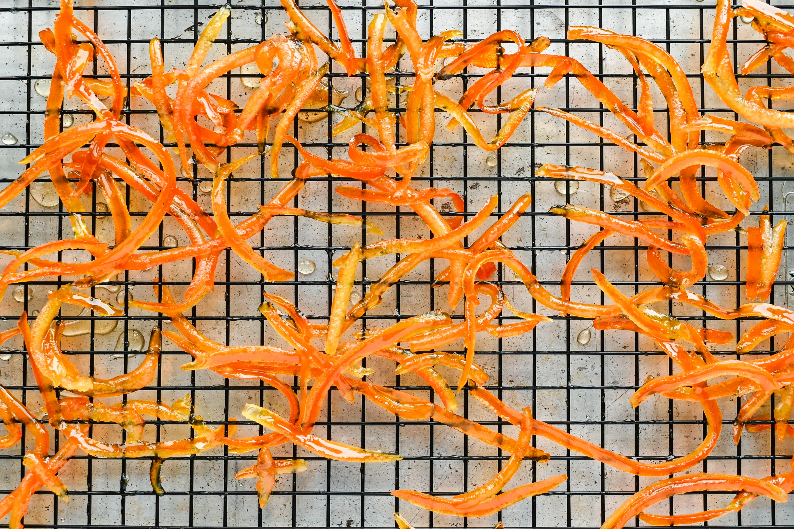 Shiny candied orange peels spread out on a wire cooling rack, drying after being cooked in sugar syrup.