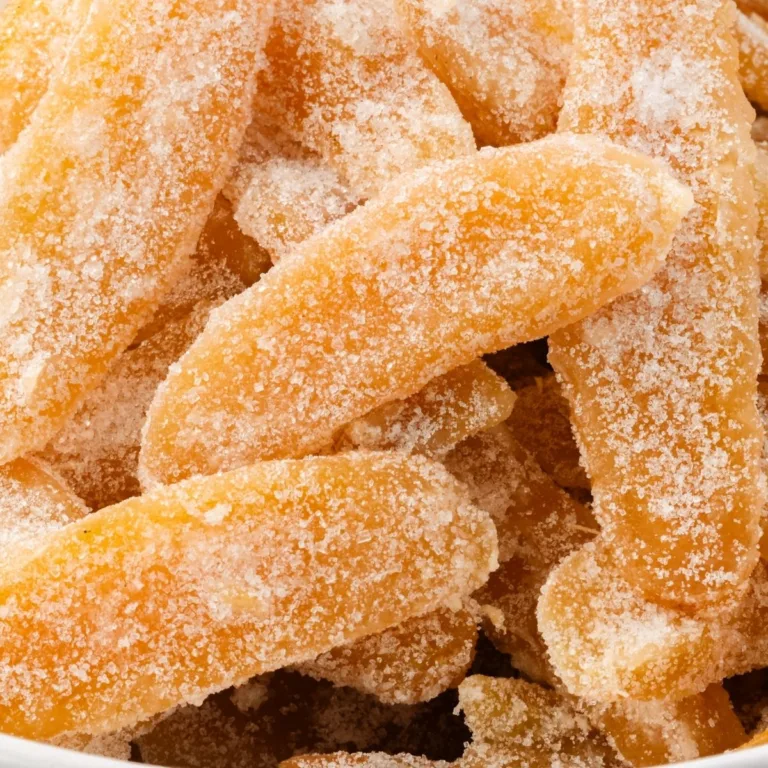 Close-up of homemade candied ginger pieces coated in sparkling sugar crystals, showing their chewy texture and bright golden color.