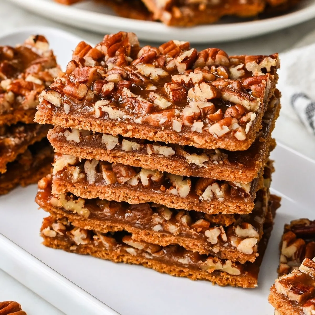 Stacked pieces of pecan pie bark made with graham cracker toffee, brown sugar, butter, and chopped pecans on a white plate.