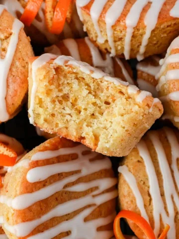Halved sourdough discard orange muffin resting on glazed muffins below, showing the soft, tender crumb and bright orange zest throughout.