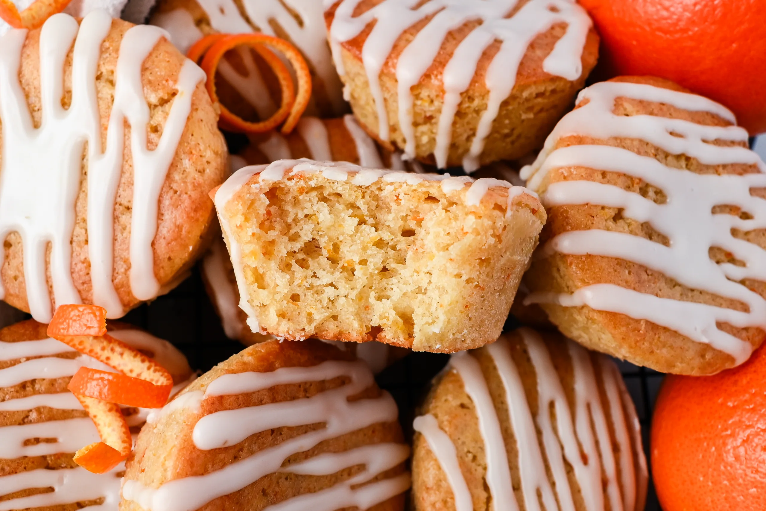 Freshly baked sourdough discard orange muffins topped with orange glaze, garnished with curled orange peels and whole oranges in the background.