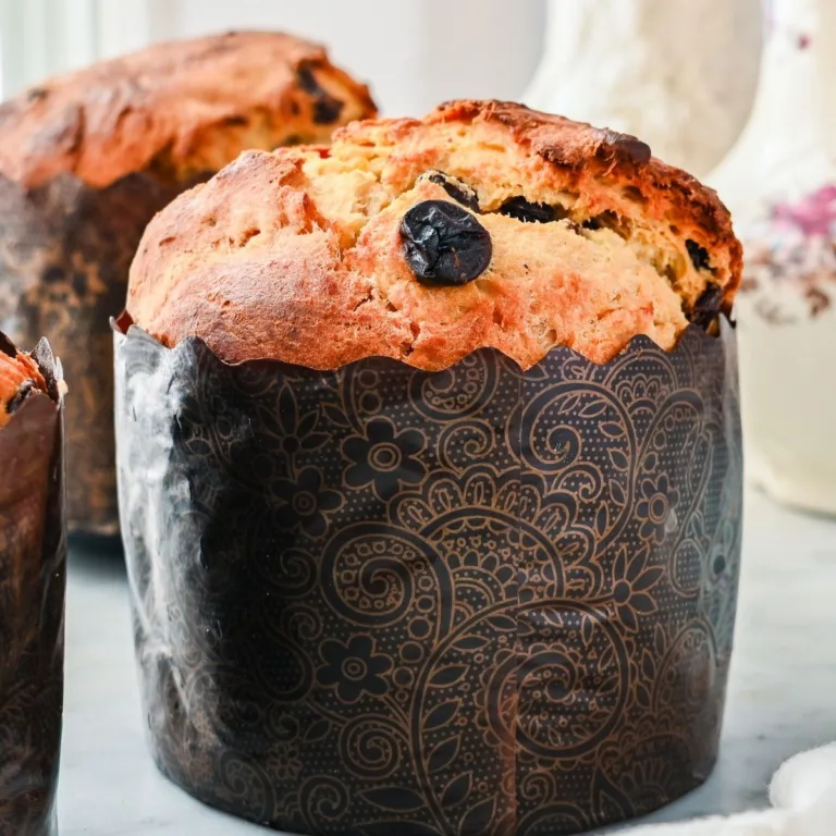 Sourdough panettone baked in a decorative paper mold, showing a golden domed top with dried fruit baked into the crust.