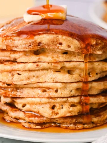 Stack of whole wheat pancakes made with fresh milled flour, topped with butter and maple syrup dripping down the sides.