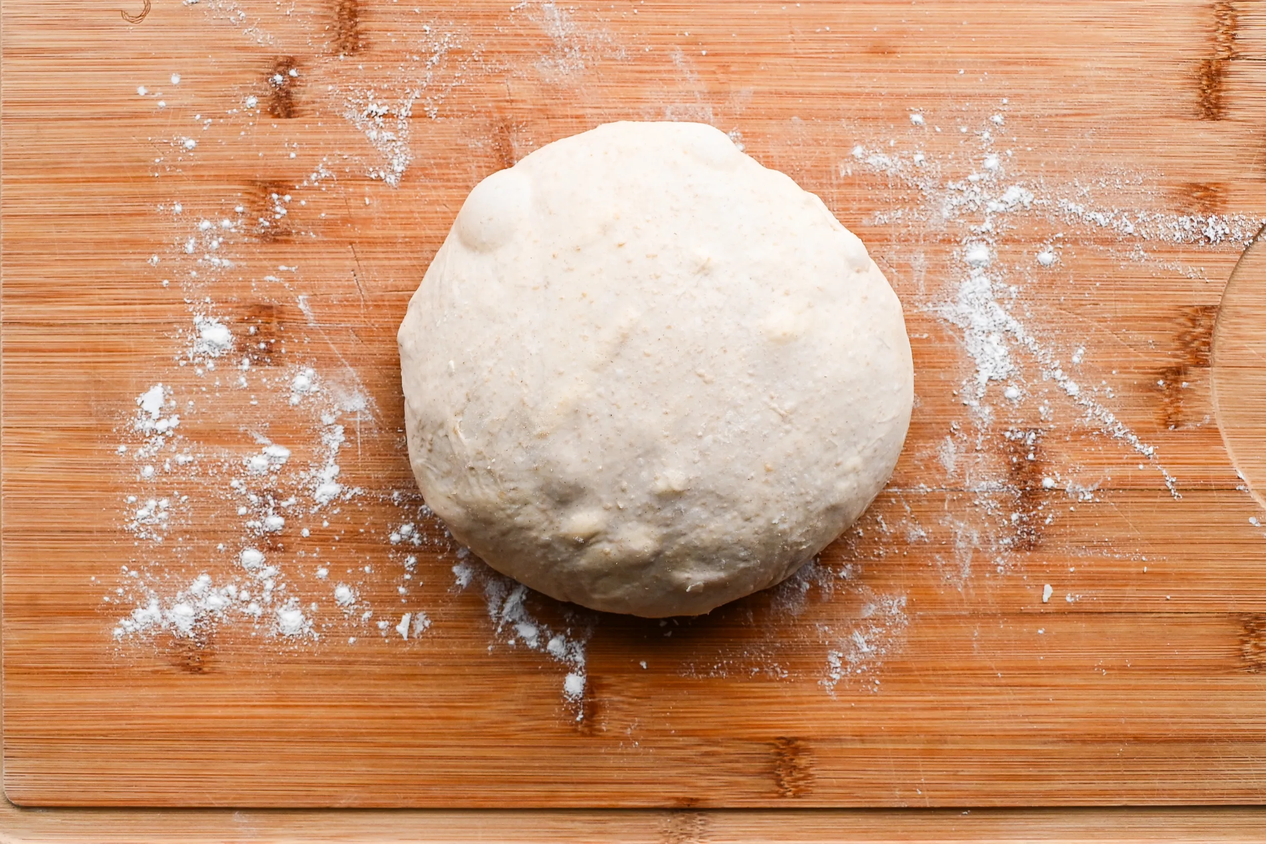 Smooth, round ball of sourdough sandwich bread dough resting on a floured wooden cutting board before the first rise.