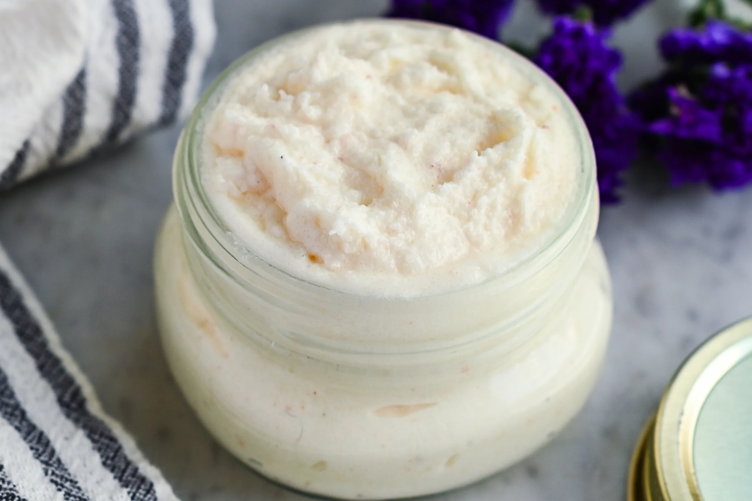 Finished tallow foot scrub in a glass jar styled with a towel and dried flowers for natural skincare.