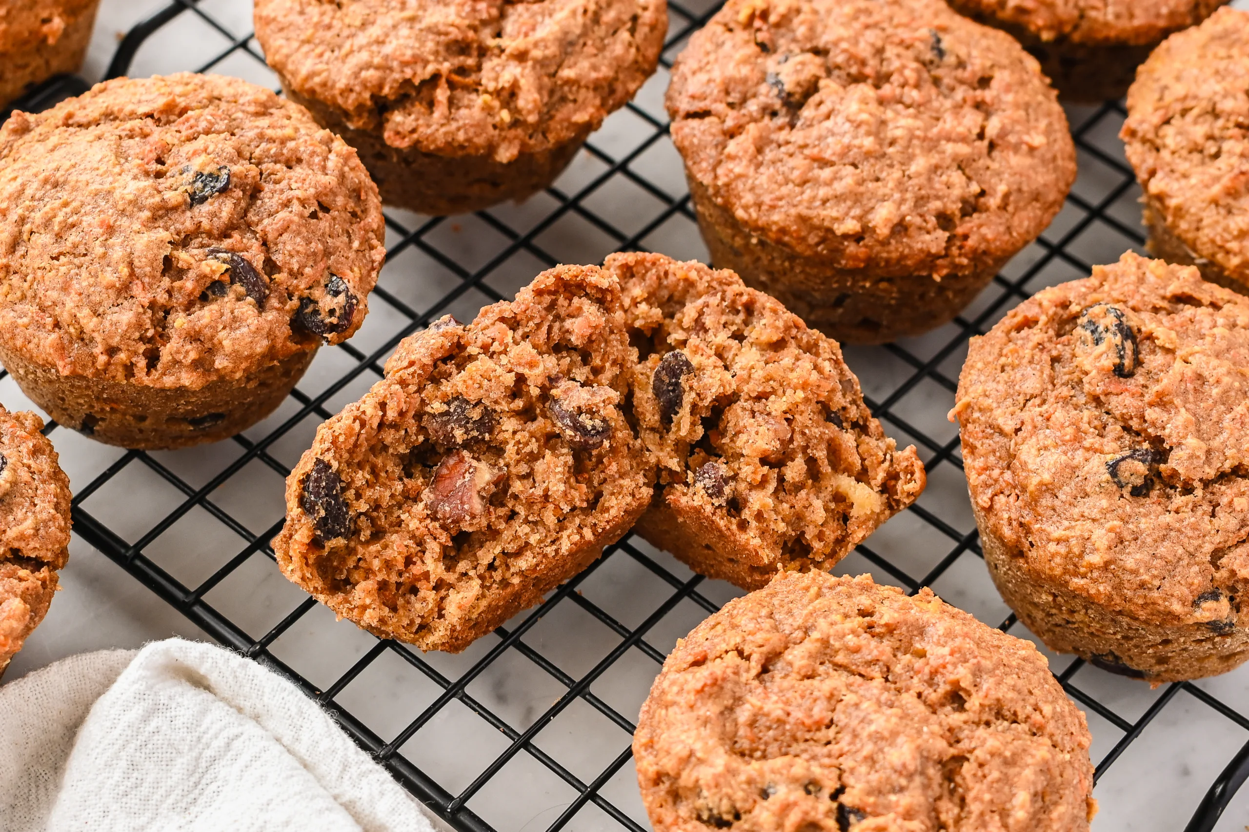 Fresh milled wheat sourdough morning glory muffins cooling on a wire rack, with one muffin split open to show the moist interior filled with fruit and nuts.