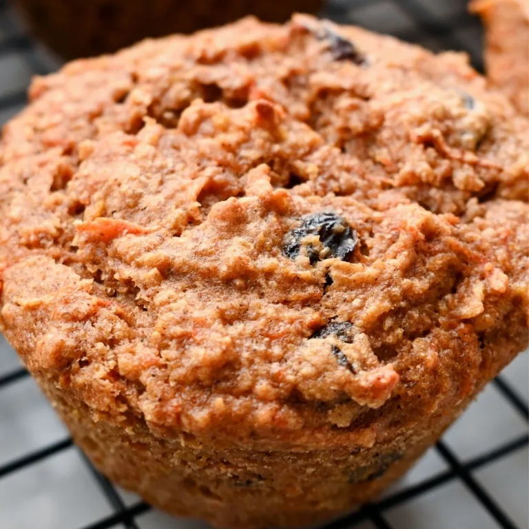 Close-up of a healthy sourdough morning glory muffin made with fresh milled wheat, showing a rustic domed top with visible raisins and grated carrot.