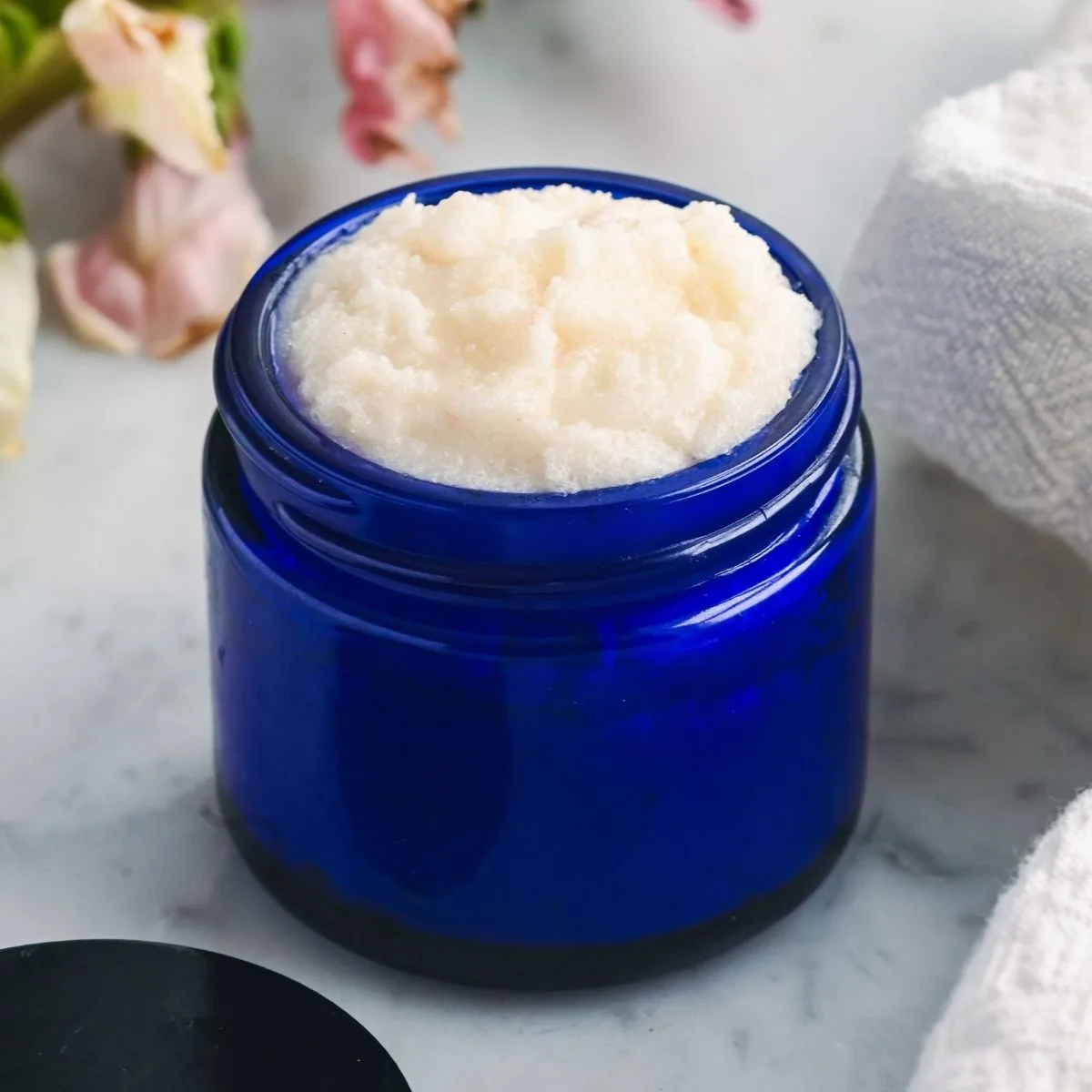 Finished homemade tallow face scrub with a soft, whipped sugar texture stored in a blue glass jar, ready for gentle facial exfoliation.