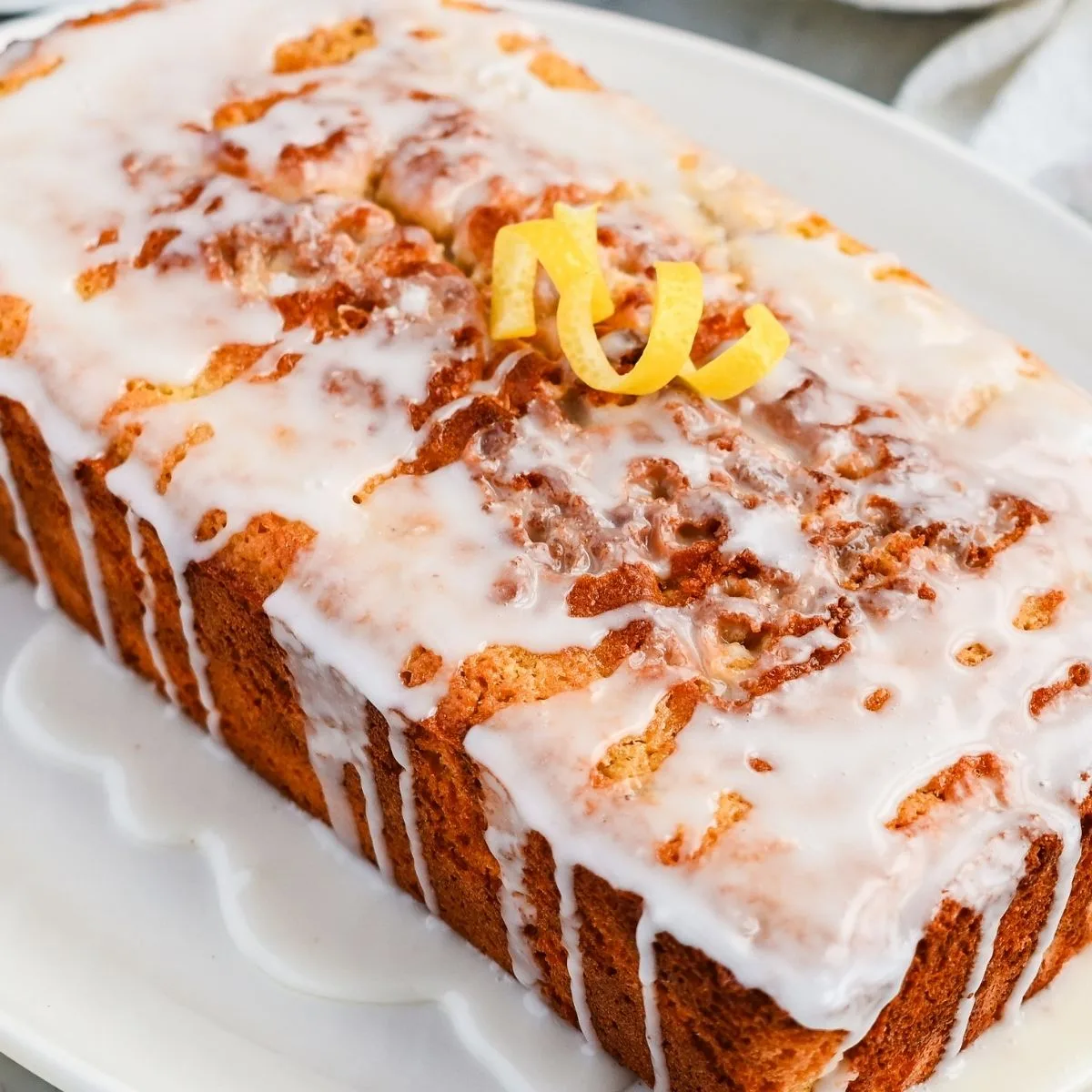 Side perspective of glazed lemon quick bread highlighting the thick lemon icing dripping down the crust.