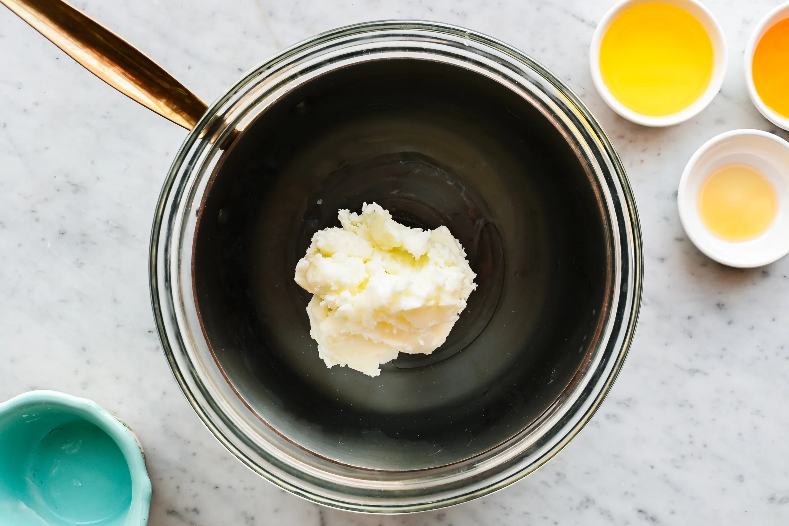 Beef tallow beginning to soften in a glass bowl as it warms gently for a face cream recipe.