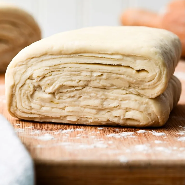 Close-up of traditional homemade puff pastry dough showing flaky butter layers and laminated folds, resting on a wooden board before rolling and baking.