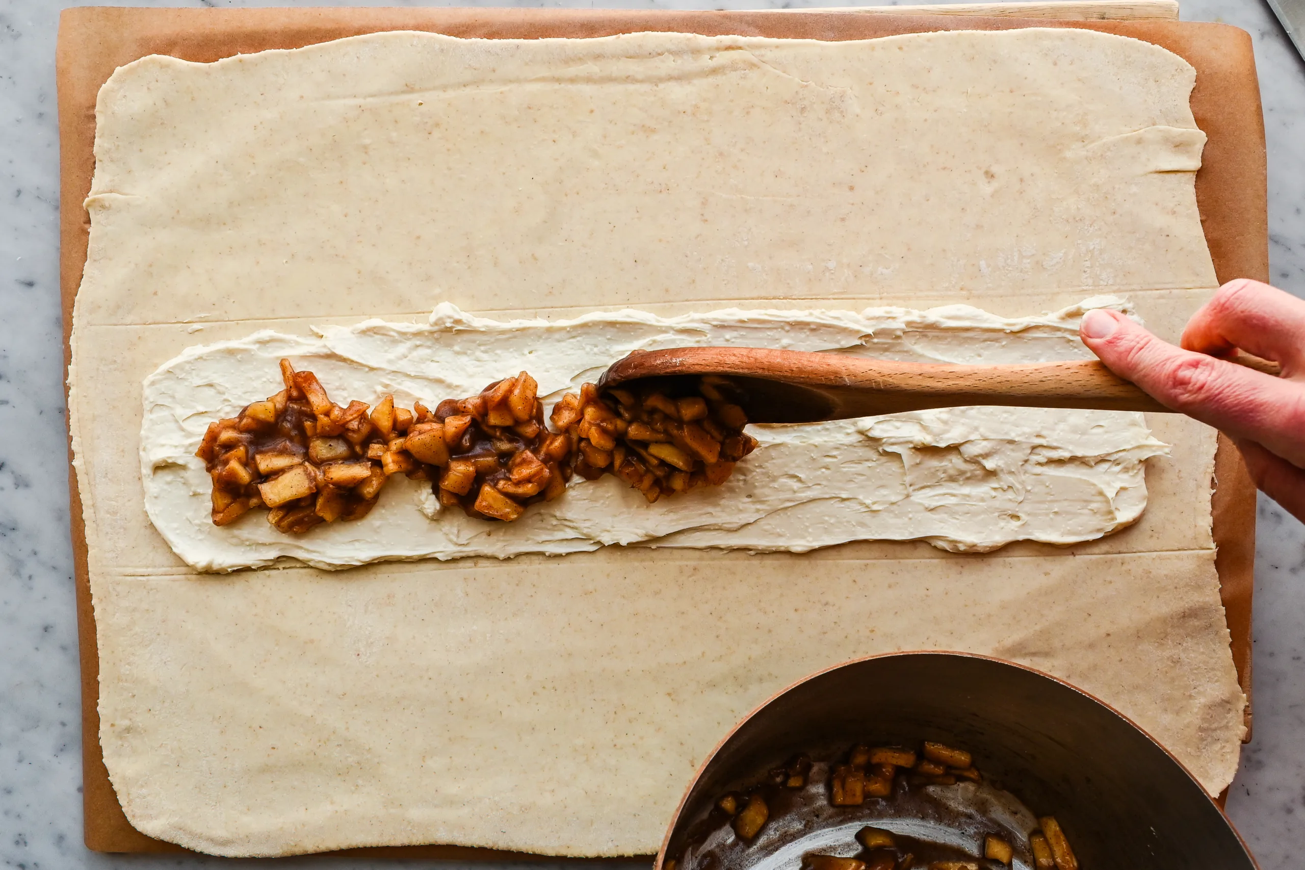Cooked cinnamon apple filling spooned over cream cheese layer on puff pastry.