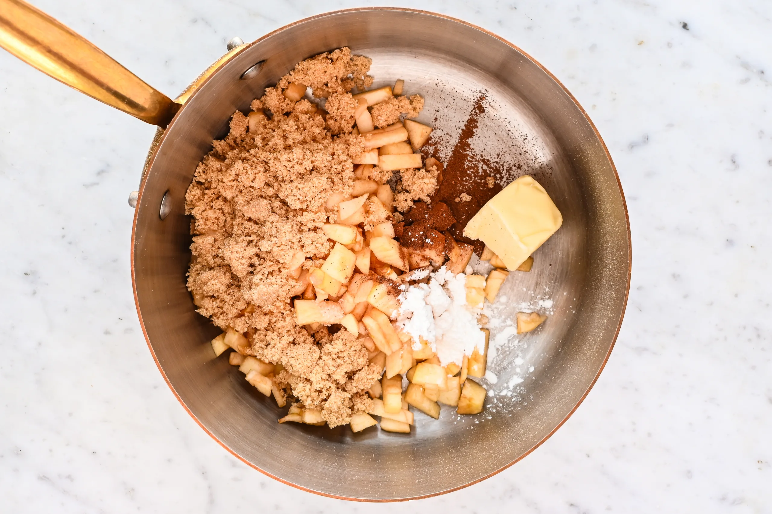 Chopped apples, brown sugar, cinnamon, butter, and cornstarch cooking in a saucepan for braided apple cream cheese puff pastry Danish.