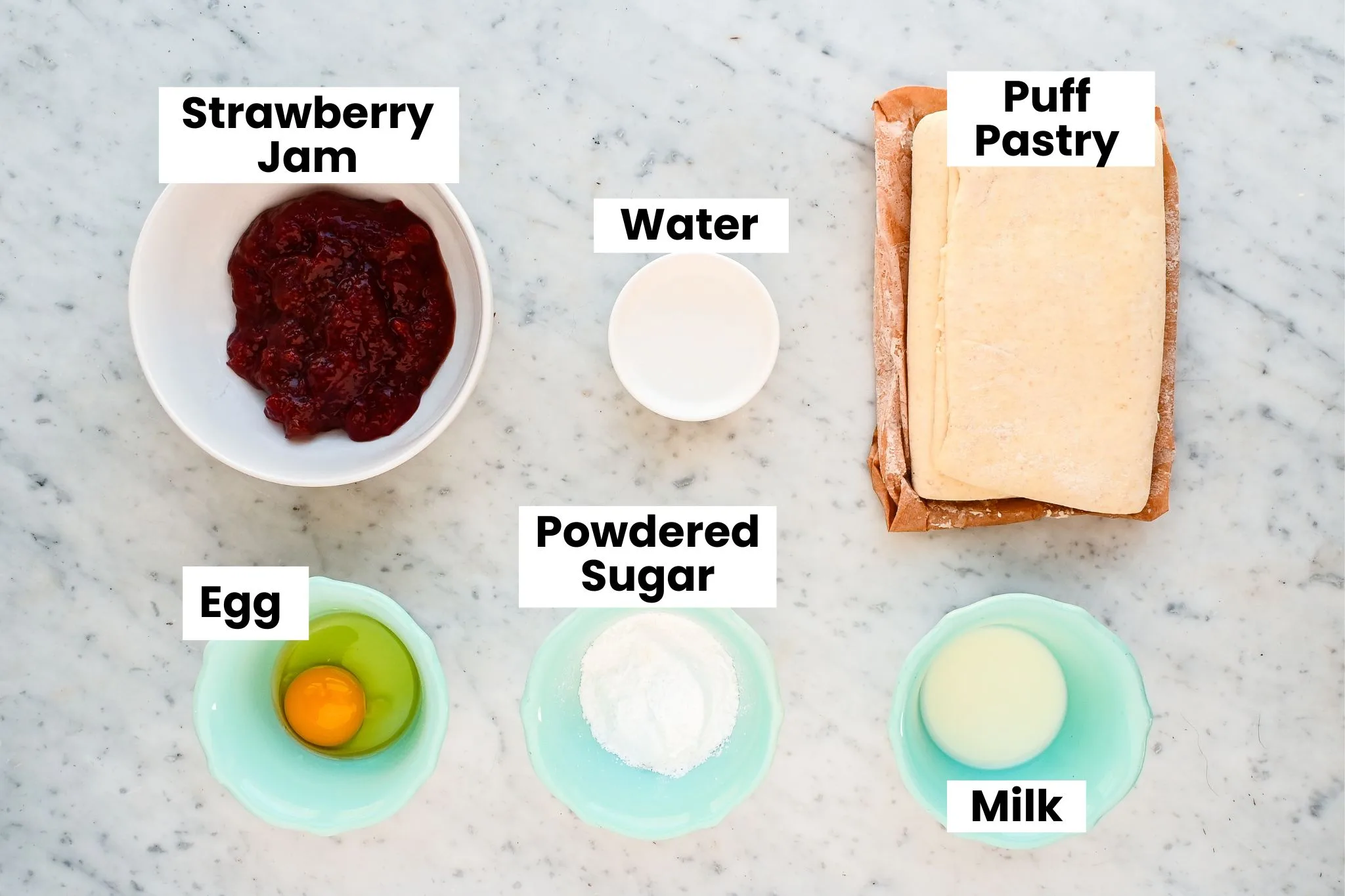 Ingredients for old-fashioned strawberry Danish pastry arranged on marble counter including puff pastry sheets, strawberry jam, egg, flour, and milk.