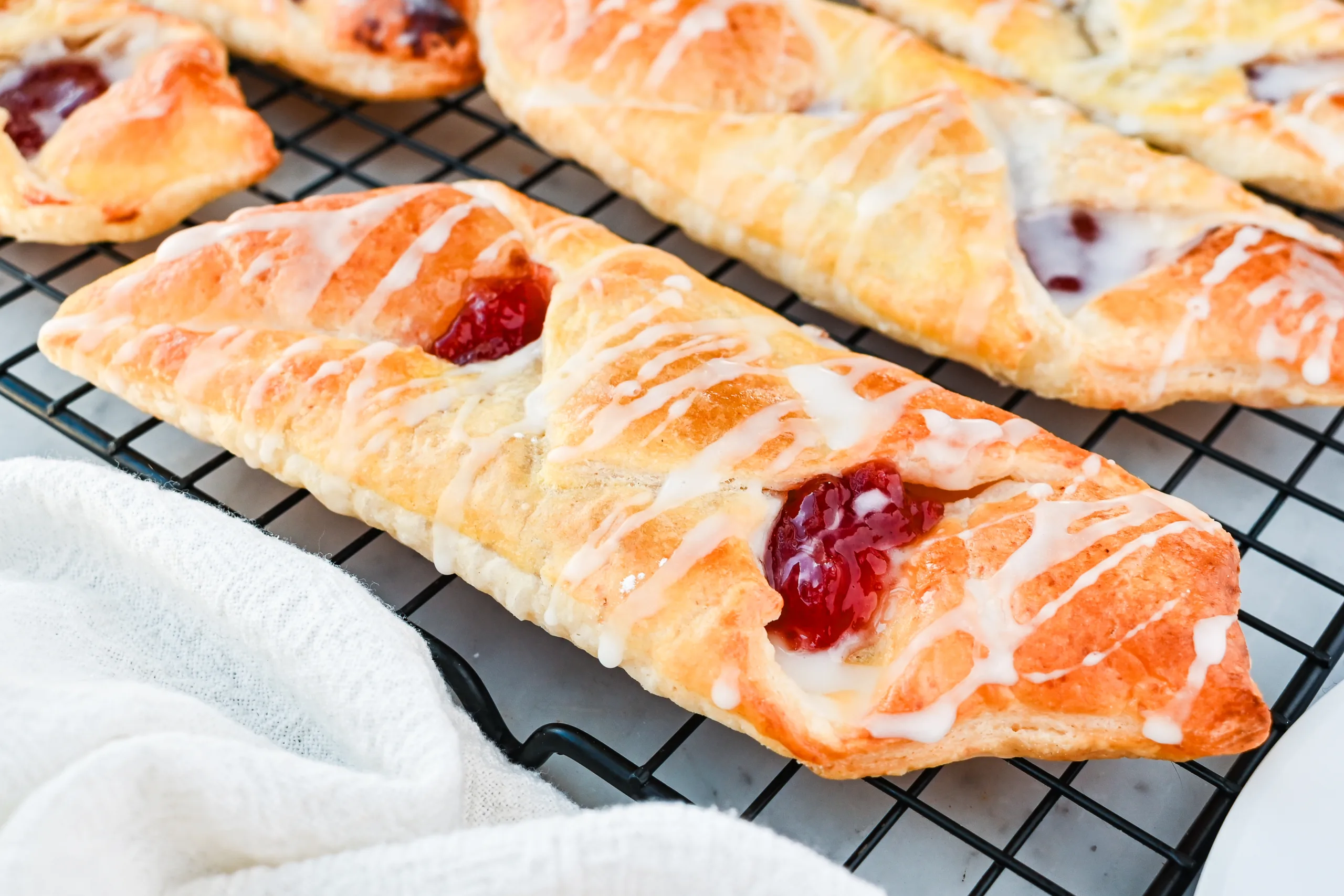 Golden brown strawberry Danish pastries cooling on wire rack with flaky homemade puff pastry layers visible.