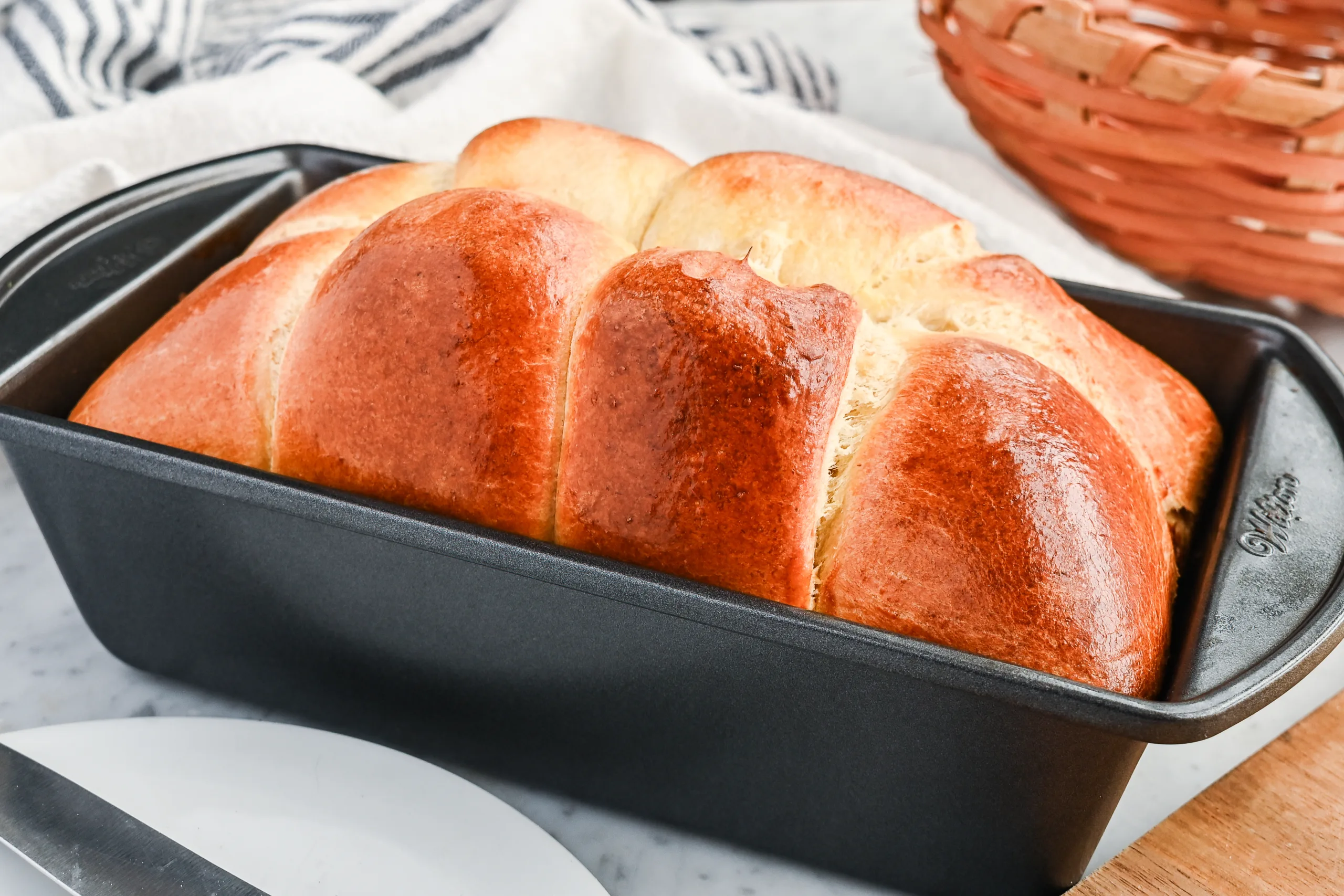 Freshly baked sourdough brioche loaf in a loaf pan with a glossy, golden brown crust.