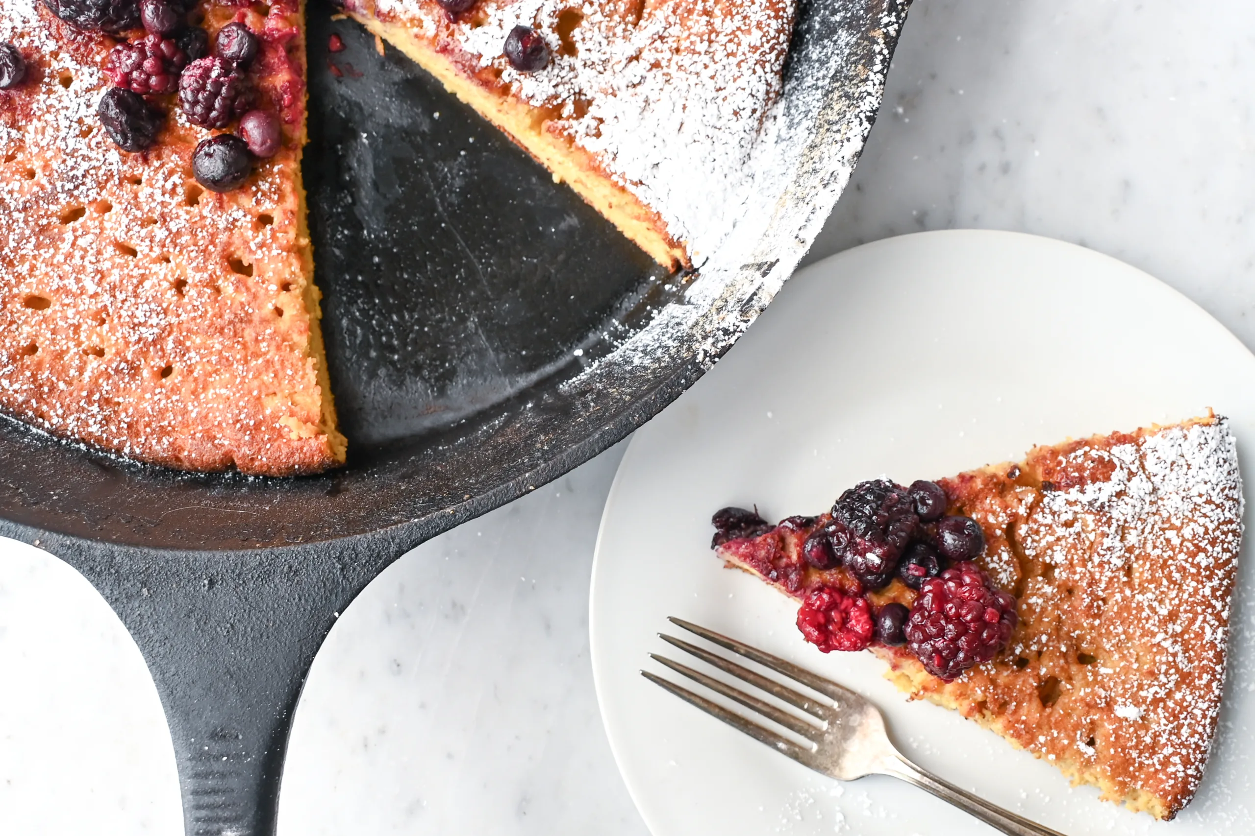 Skillet sourdough German pancake with powdered sugar and fresh berries, photographed from above.
