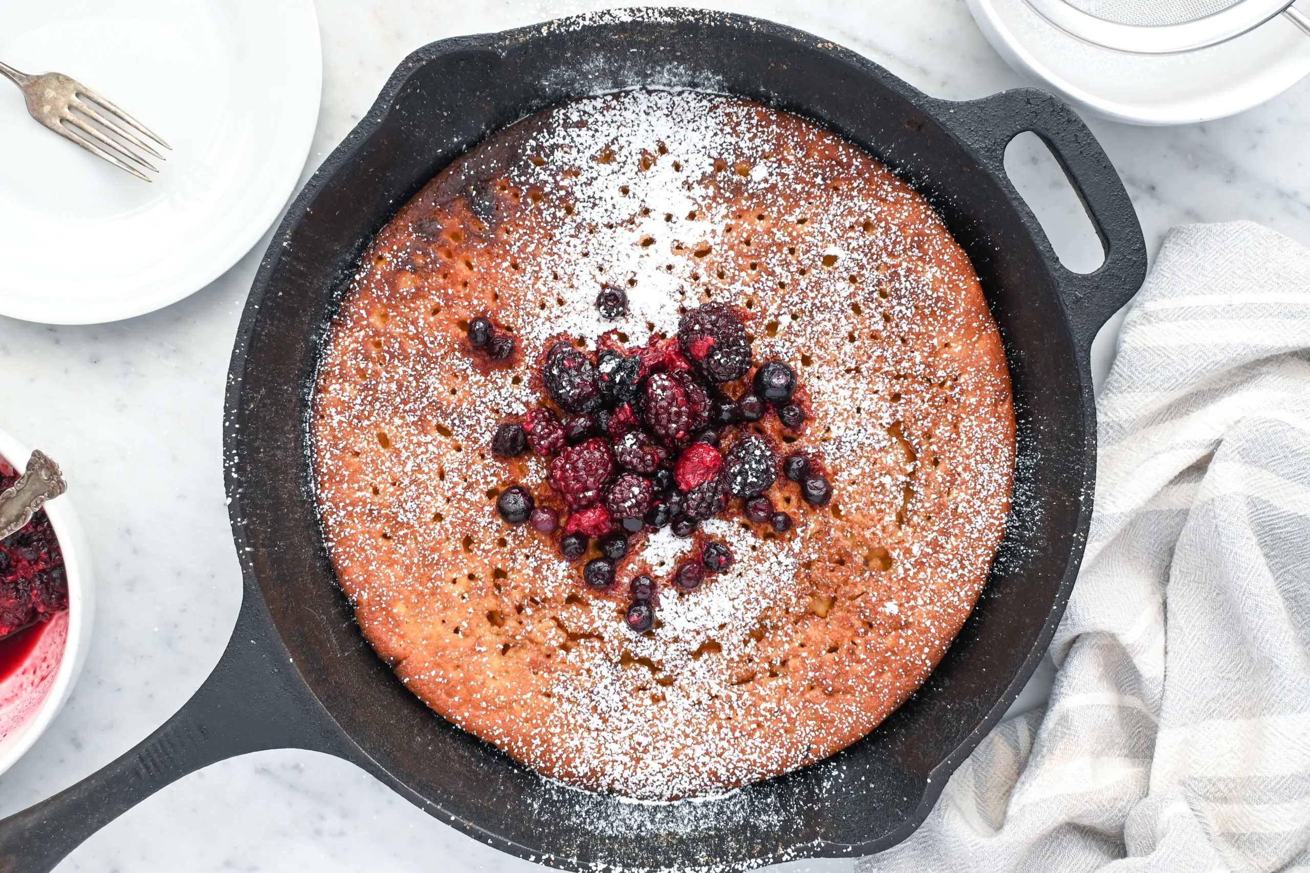 German pancake made with sourdough starter topped with powdered sugar and mixed berries in a cast iron pan.