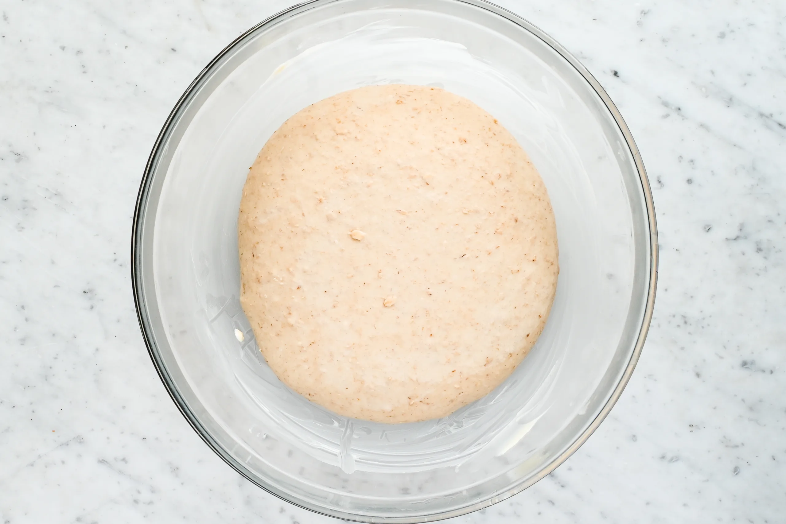 Sourdough oat dough resting in a lightly greased glass bowl before bulk fermentation, showing a smooth and cohesive texture.