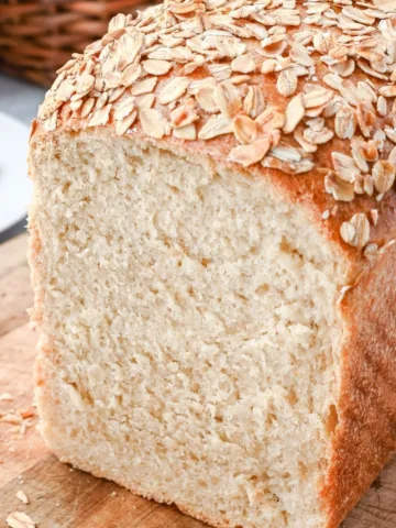Soft honey oat sourdough sandwich loaf sliced to show a tender, even crumb and golden crust topped with toasted rolled oats.