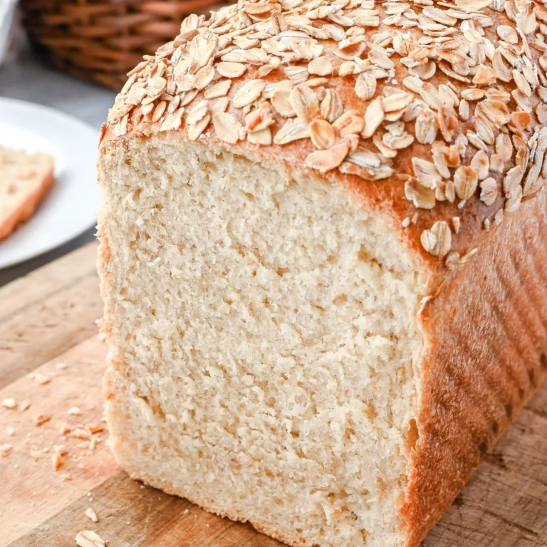 Soft honey oat sourdough sandwich loaf sliced to show a tender, even crumb and golden crust topped with toasted rolled oats.
