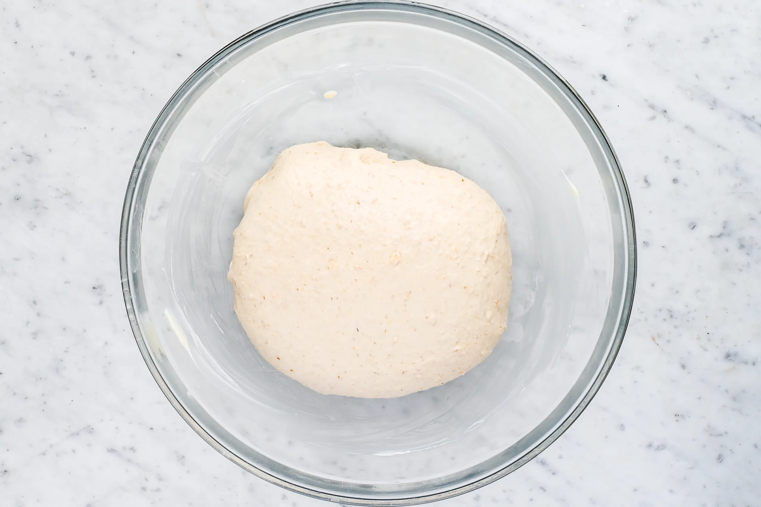 Smooth sourdough oatmeal bread dough resting in a greased glass bowl before bulk fermentation for a soft honey oat sandwich loaf.