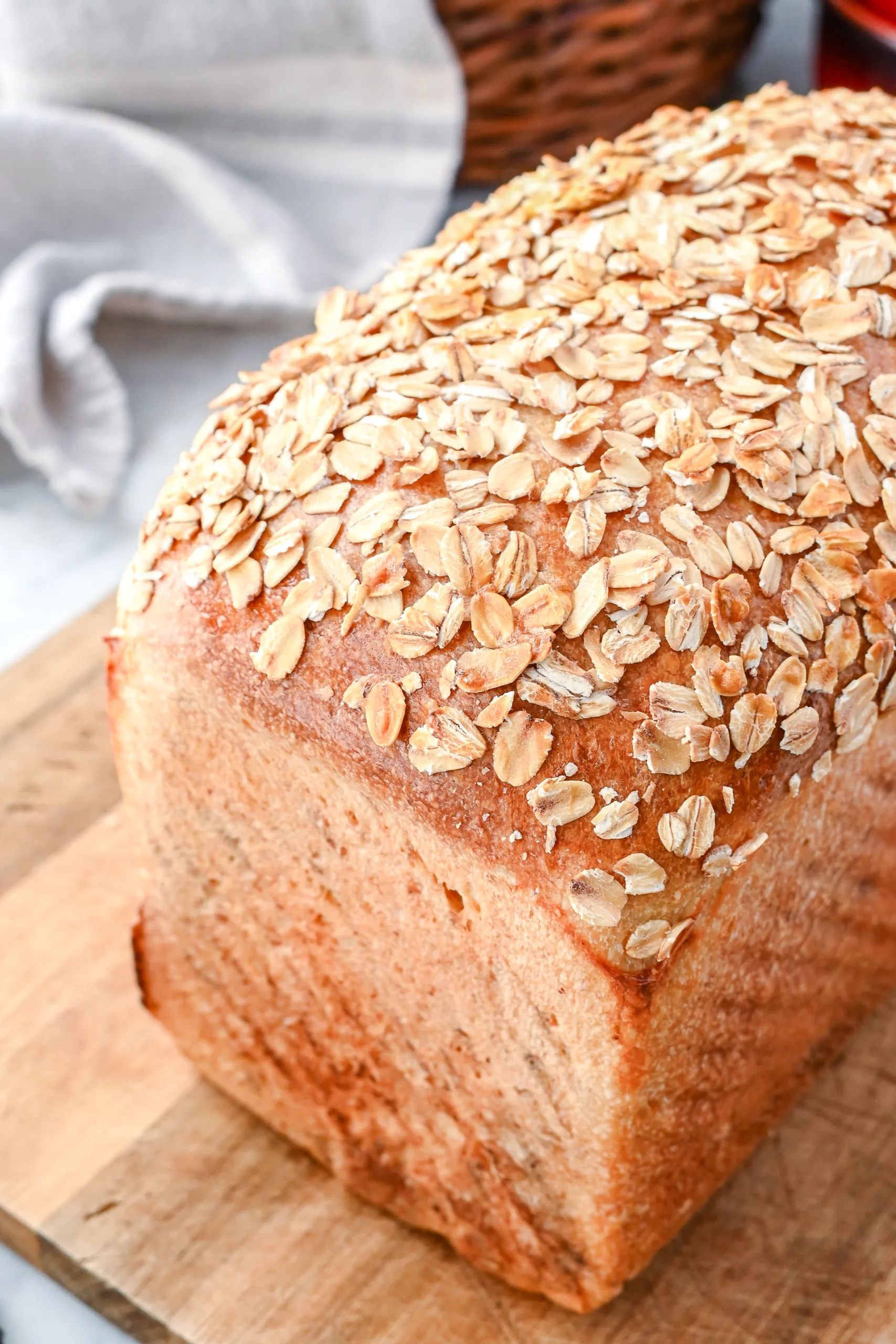 Golden brown sourdough oatmeal sandwich loaf topped with oats, photographed on a wooden board with a rustic kitchen background.