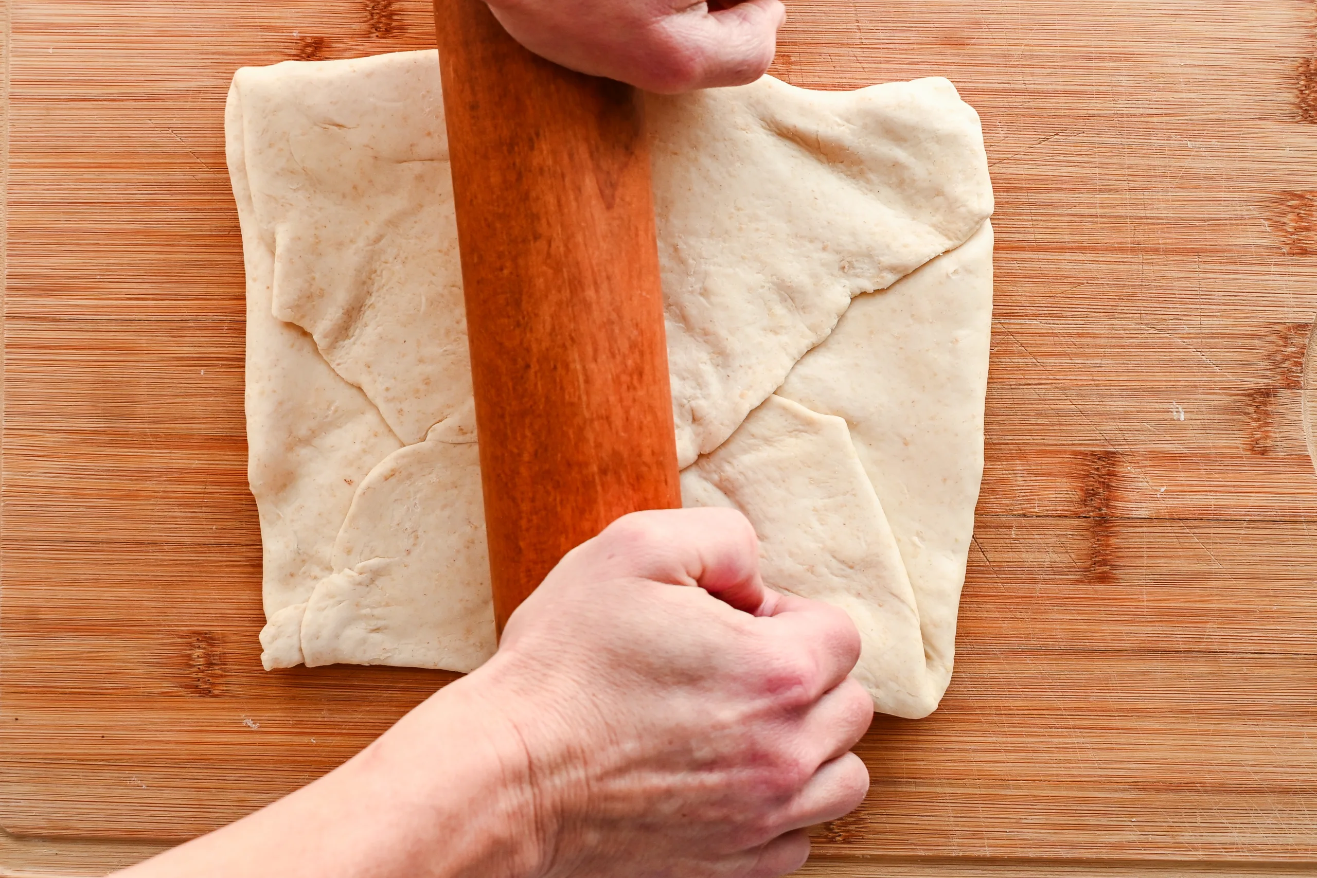 Rolling laminated sourdough puff pastry dough after folding to create thin layers of butter and dough.