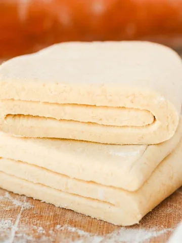 Folded sourdough puff pastry dough showing laminated layers resting on a lightly floured wooden surface before baking.