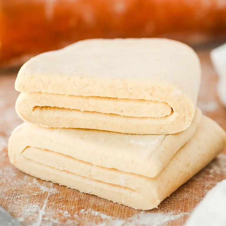 Folded sourdough puff pastry dough showing laminated layers resting on a lightly floured wooden surface before baking.