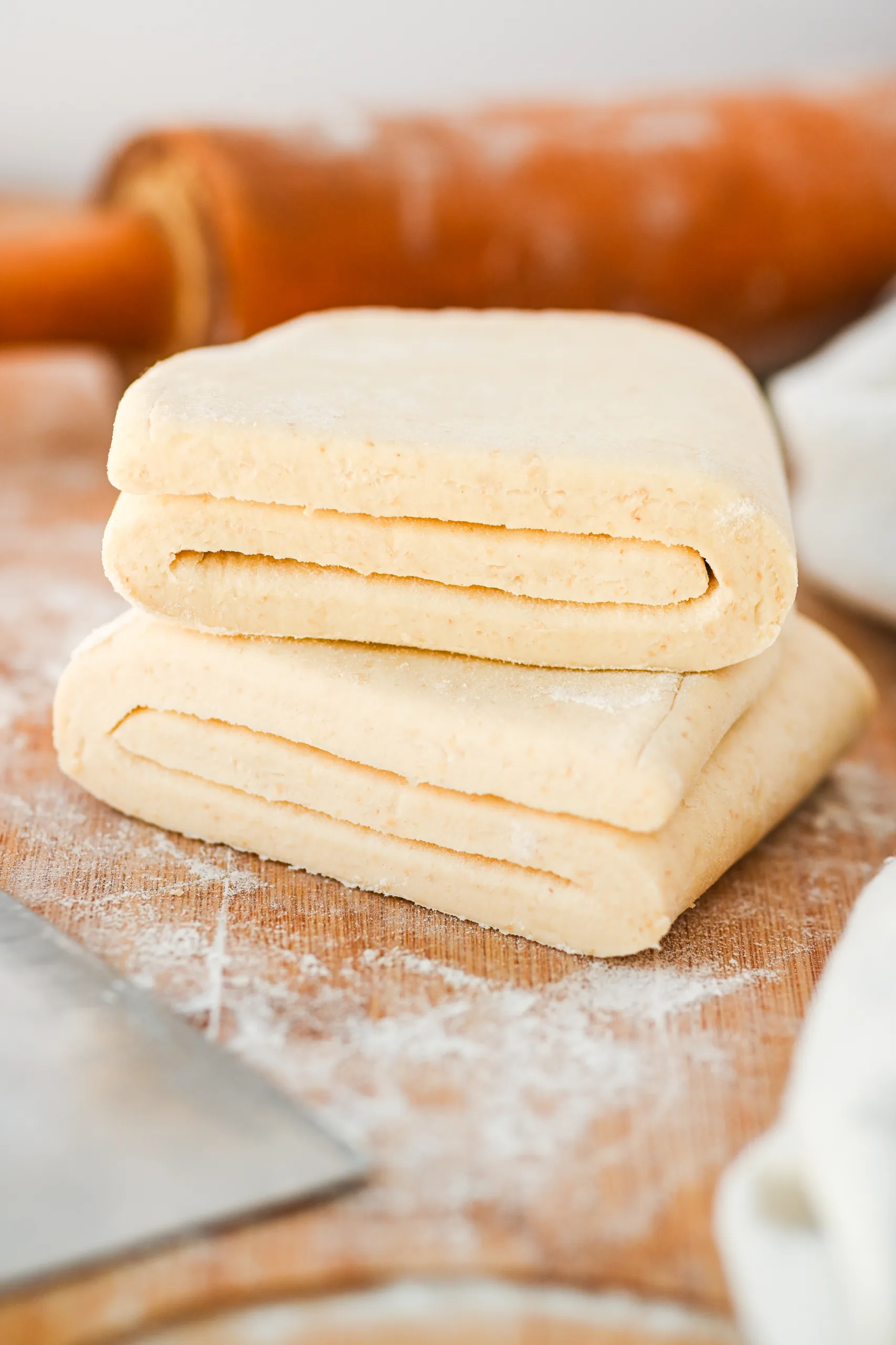 Stacked sourdough puff pastry dough showing visible laminated layers on a lightly floured wooden surface.