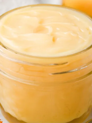 Close-up of homemade tallow balm for acne prone skin in a small glass jar, showing a smooth creamy texture and natural golden color made with simple old-fashioned ingredients.