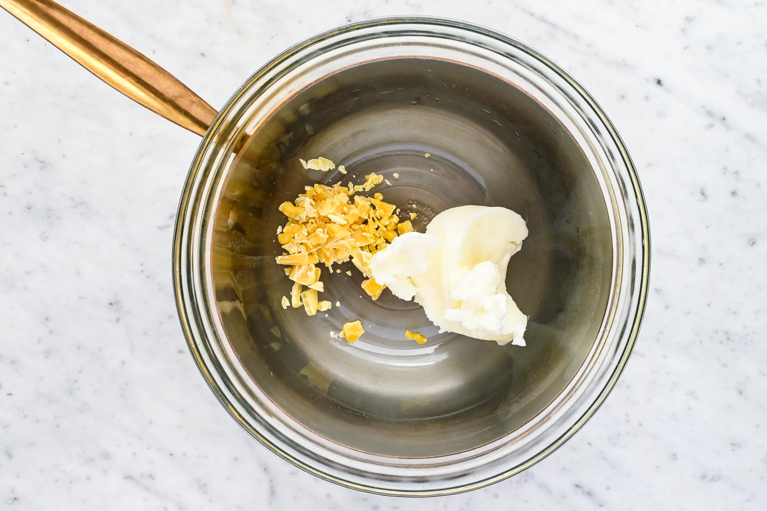 Rendered beef tallow and beeswax pellets in a glass bowl ready to be gently melted for homemade tallow balm.