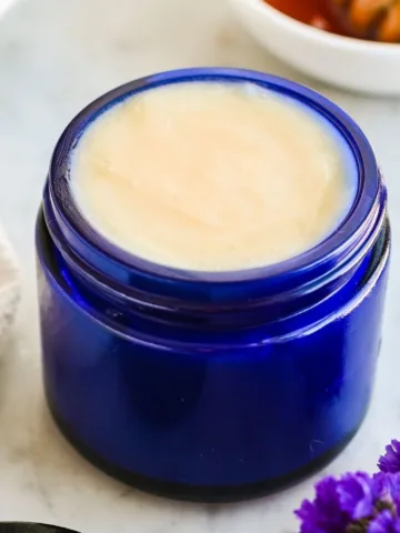 Finished homemade tallow and honey balm in a blue glass jar showing a smooth, creamy surface after setting.
