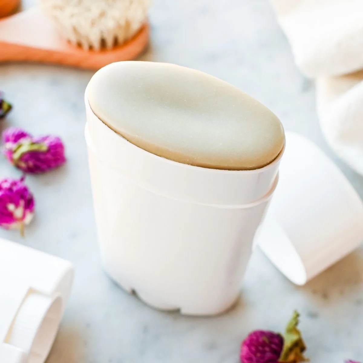 Angled view of smooth homemade tallow deodorant stick in a reusable white deodorant tube with dried flowers nearby.